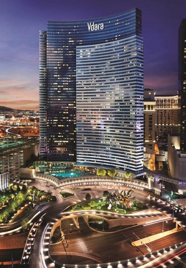A modern hotel with a curved facade, multiple floors, and a well-lit entrance area with a landscaped garden.