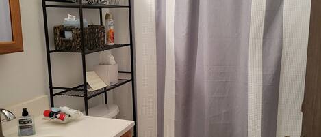 Ein Badezimmer mit einem weißen Waschbecken, Holzschränken, einer Toilette, einer Duschvorhang und einem Ablagebereich für Toilettenartikel.