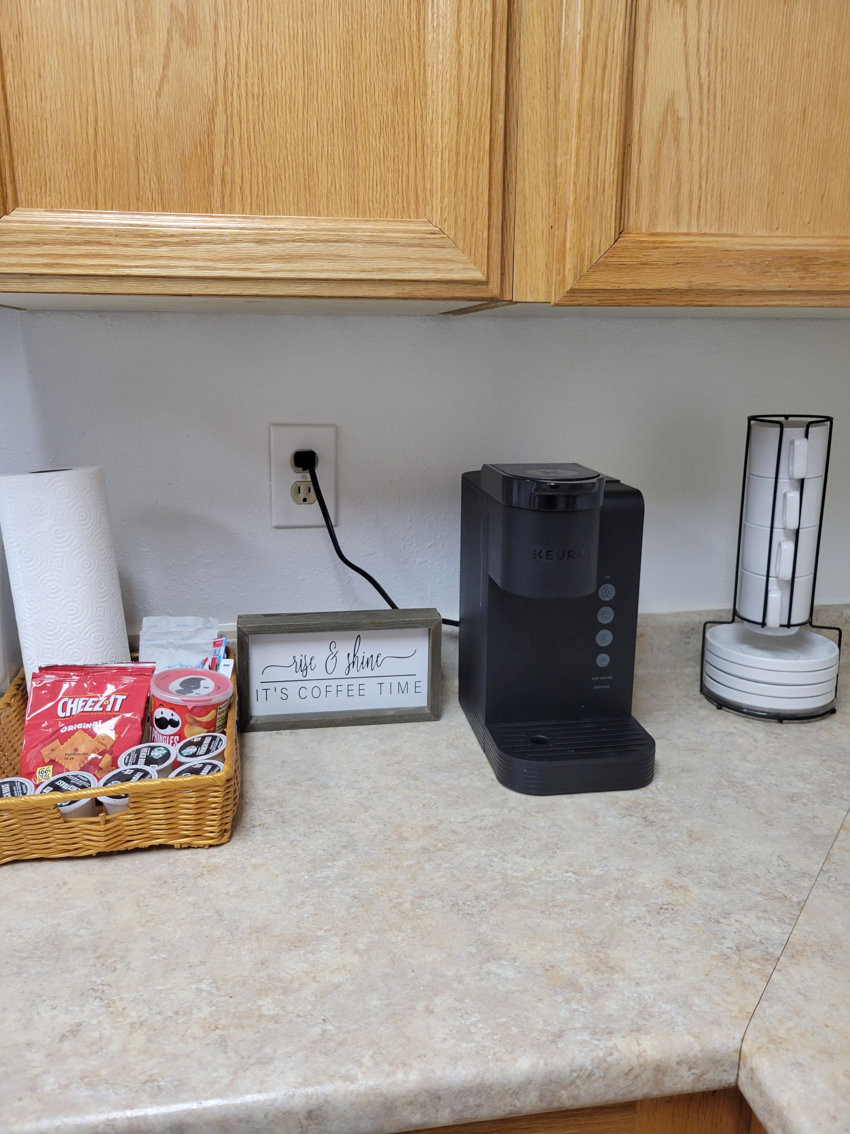 Una encimera de cocina con una cafetera, una cesta de aperitivos, un dispensador de toallas de papel y un letrero que dice 'Es hora del café'.