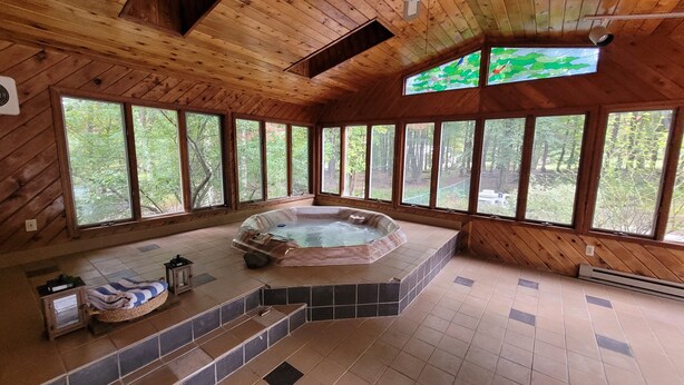 Une cabane en bois dotée d’un bain à remous, de grandes fenêtres et offrant une vue sur la forêt.