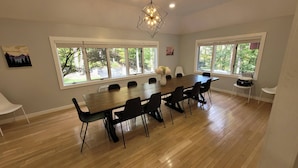 Un espace repas avec une table et des chaises en bois, de grandes fenêtres donnant sur la verdure et un luminaire au design géométrique.