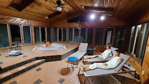 Une cabane en bois dotée d’un bain à remous, de chaises longues et de grandes fenêtres.