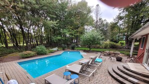 Un jardin avec une piscine, des chaises longues et un espace aménagé autour d’un foyer.