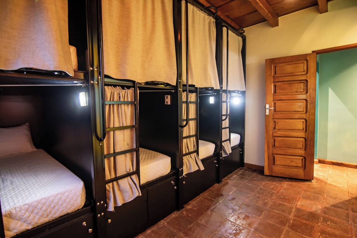 A row of bunk beds with curtains, a wooden door, and a tiled floor.