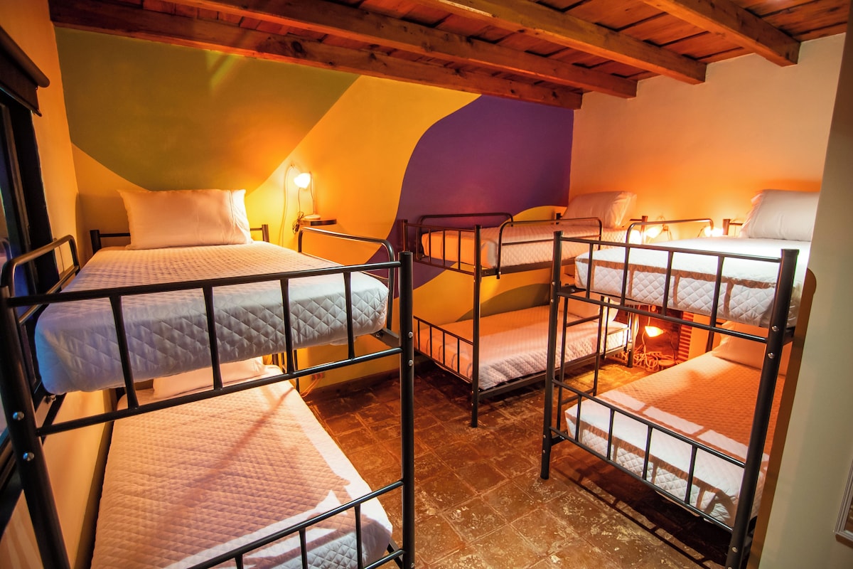 A dormitory room with bunk beds, wooden beams, and a sloped ceiling.