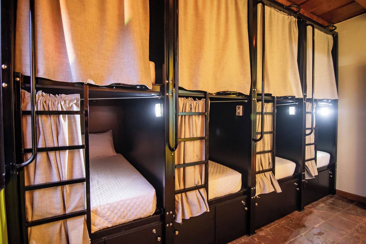 A row of bunk beds with curtains, each bed having a mattress and pillows.