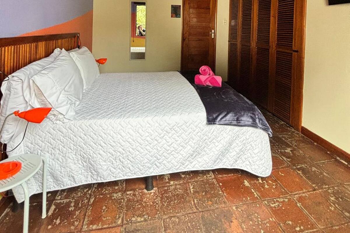A bedroom with a bed, a small table, a wooden ceiling, a door, and a window.
