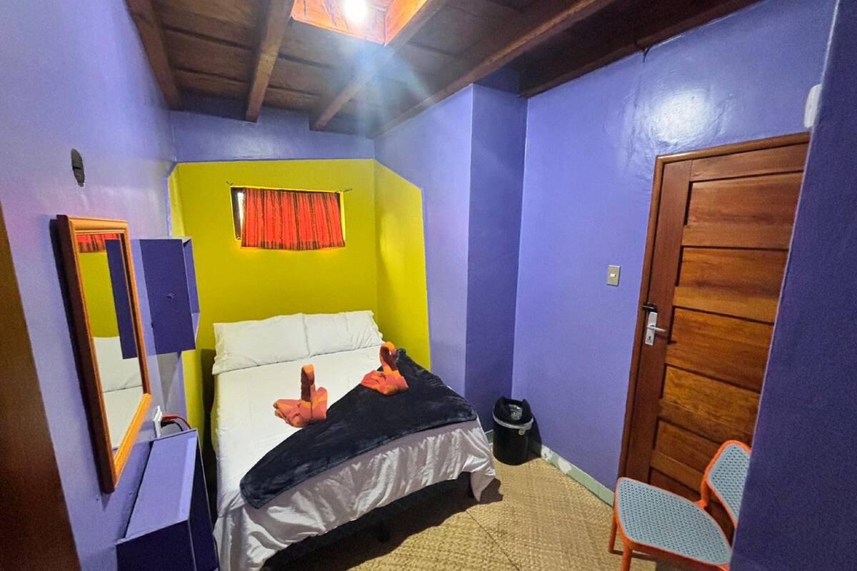 A bedroom with a bed, a chair, a mirror, a window with curtains, and a door.
