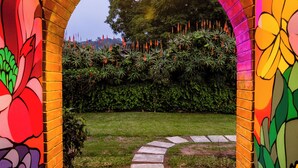 Una entrada en arco con murales coloridos, un camino de piedra y un jardín al fondo.