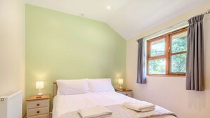 Une chambre à coucher avec un lit, deux tables de chevet, une fenêtre avec des rideaux et un radiateur.