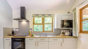Une cuisine moderne avec des meubles blancs, un four encastré, un four à micro-ondes et une fenêtre donnant sur un espace verdoyant.
