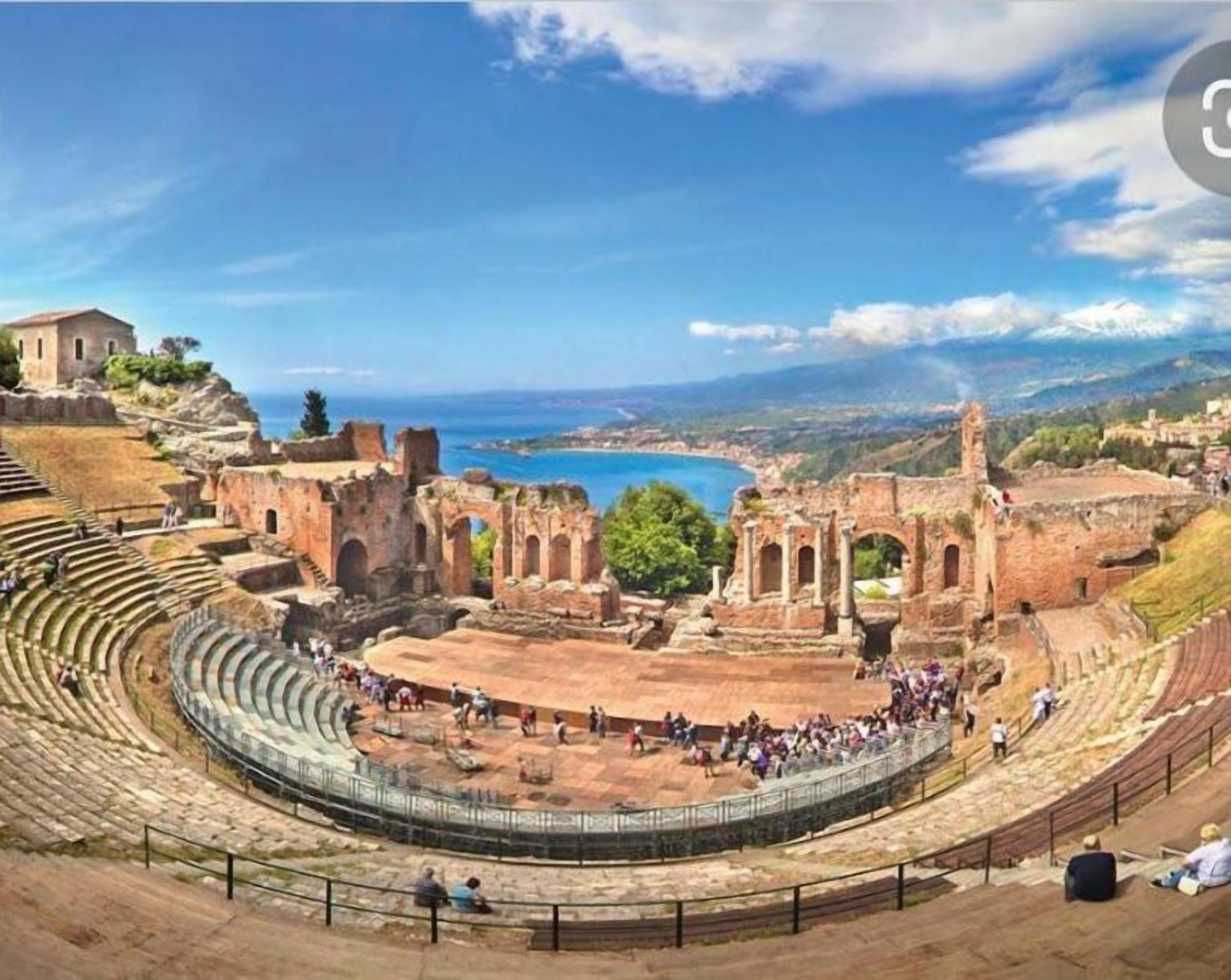 An ancient amphitheater with tiered seating and ruins in the background.