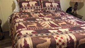 A bed with a patterned quilt featuring animal designs, a bedside table, and a lamp.