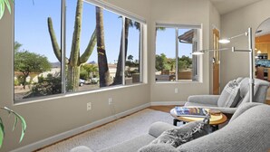 A spacious living room with large windows offering a view of cacti and palm trees.