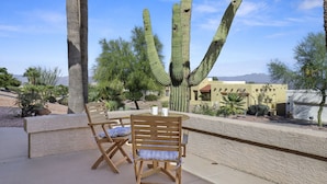 An outdoor seating area with wooden chairs and a table, surrounded by cacti and desert vegetation.