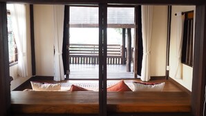 Een traditionele Japanse kamer met tatami vloerbedekking, een schuifdeur naar een buitenbalkon en een houten bank.