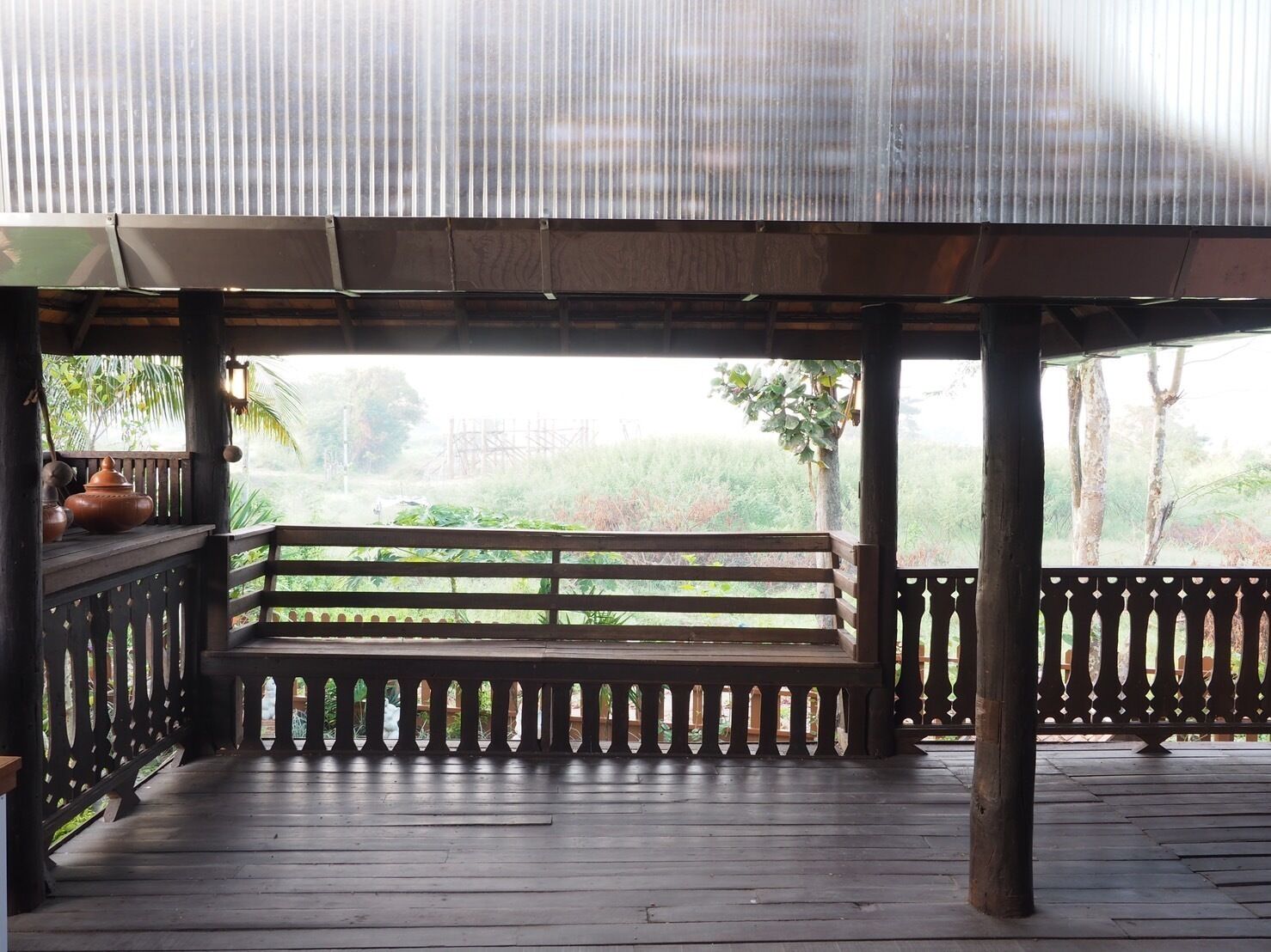 Una terraza de madera con un banco, rodeada por una barandilla, con vistas a un paisaje verde exuberante.