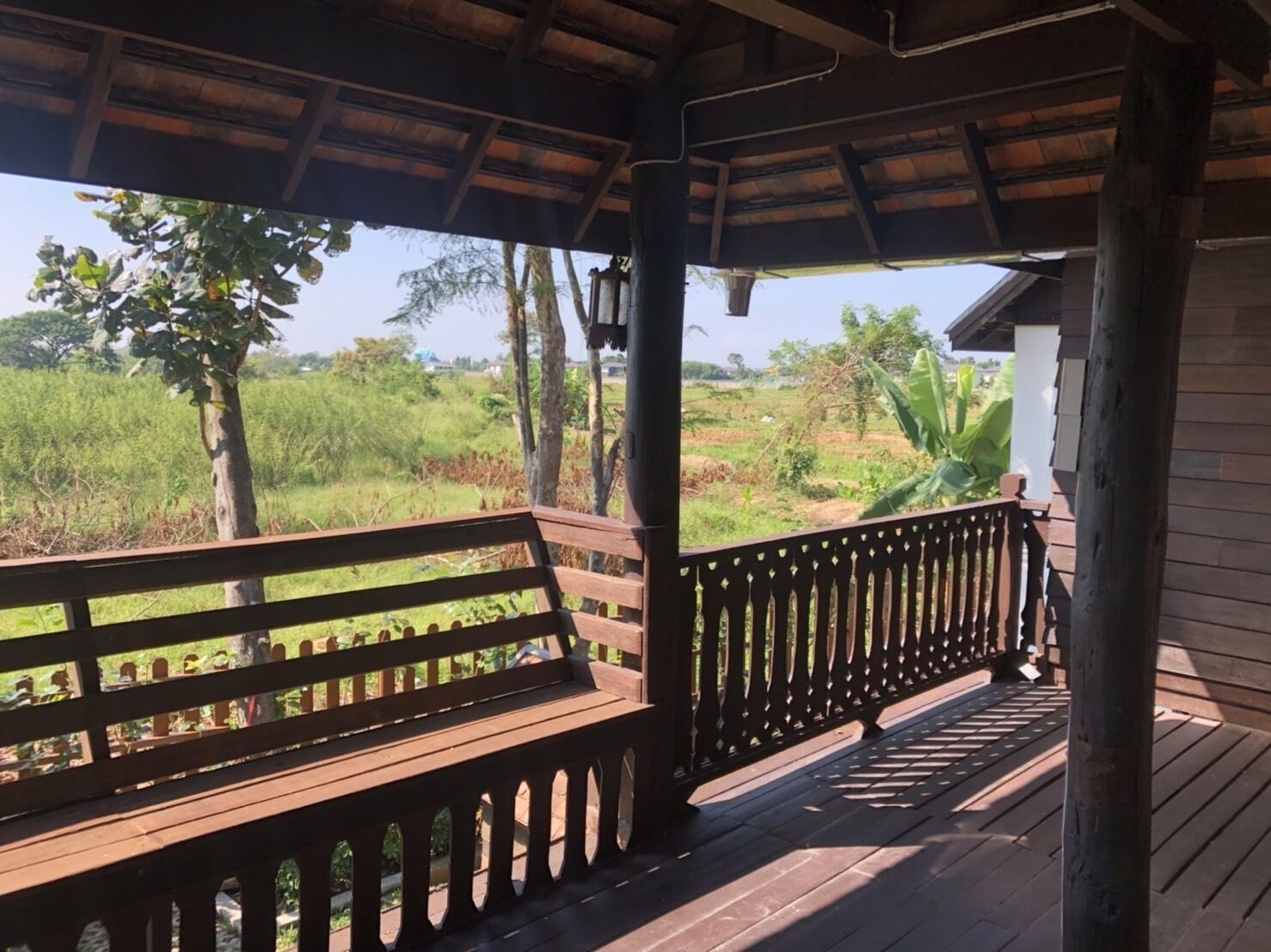 A wooden deck with a bench and railing, overlooking a lush landscape with trees and fields.
