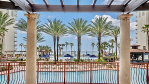 A pool area with palm trees, a pool, and a view of the ocean.
