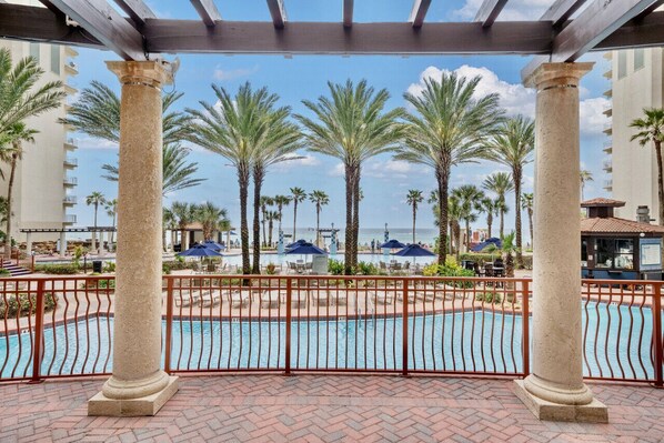 A pool area with palm trees, a pool, and a view of the ocean.