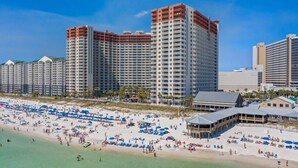 A beachfront hotel with multiple high-rise buildings, a sandy beach with umbrellas, and a clear blue sky.