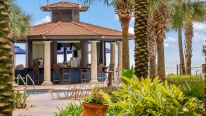 A covered outdoor bar with a pool, surrounded by palm trees and plants.
