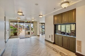 Enter a stylish lobby with a herringbone-patterned floor and a large aquarium, leading to a poolside view.