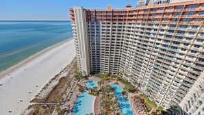 A high-rise hotel with a beachfront pool area, multiple swimming pools, and a beach.