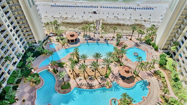 A resort with multiple swimming pools, palm trees, and beach umbrellas.