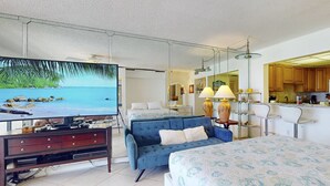 Habitación de hotel con televisor grande, sofá, cama y área de cocina.