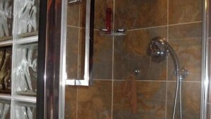 Une douche avec une porte en verre, un pommeau de douche à main et un porte-serviettes.