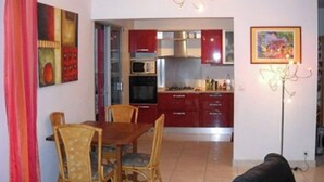 Un coin repas avec une table et des chaises en bois, une cuisine avec des placards rouges, un four à micro-ondes et un lustre.
