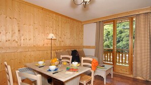 Um quarto com painéis de madeira, mesa de jantar posta para dois, uma luminária e vista para o verde pela janela.