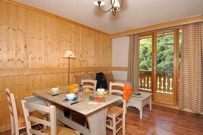 Ein Zimmer mit Holzvertäfelung, einem für zwei Personen gedeckten Esstisch, einer Lampe und Blick auf Grün durch ein Fenster.