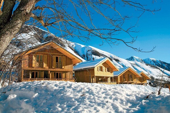 A wooden chalet with a snow-covered roof, surrounded by snow-covered mountains.