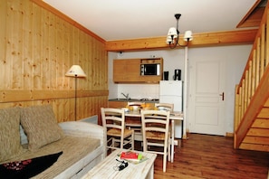 Un interior de madera acogedor con un sofá, una mesa de comedor, sillas, una zona de cocina con un microondas y una escalera.