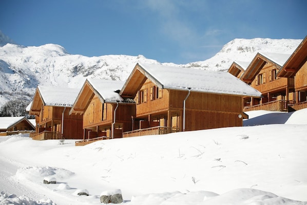 Un hilero de cabañas de madera con techos inclinados, frente a un paisaje montañoso nevado.