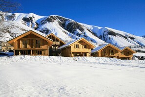 Ein Chalet-Hotel aus Holz mit mehreren Zimmern vor einer verschneiten Berglandschaft.