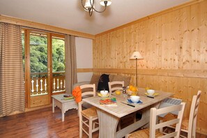 Una habitación con paneles de madera, una mesa de comedor para dos personas, una silla, una mesita y una lámpara.