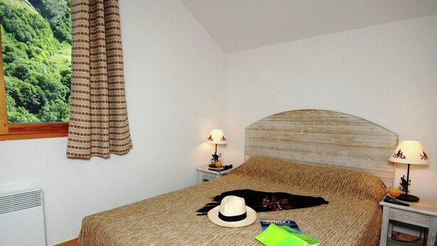 Um quarto com uma cama, duas mesas de cabeceira com abajures, uma janela com cortinas e um radiador.