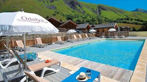 Área de piscina com espreguiçadeiras, guarda-sóis e cabanas de madeira ao fundo.