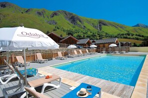 Ein Poolbereich mit Liegestühlen, Sonnenschirmen und Holzhütten im Hintergrund.