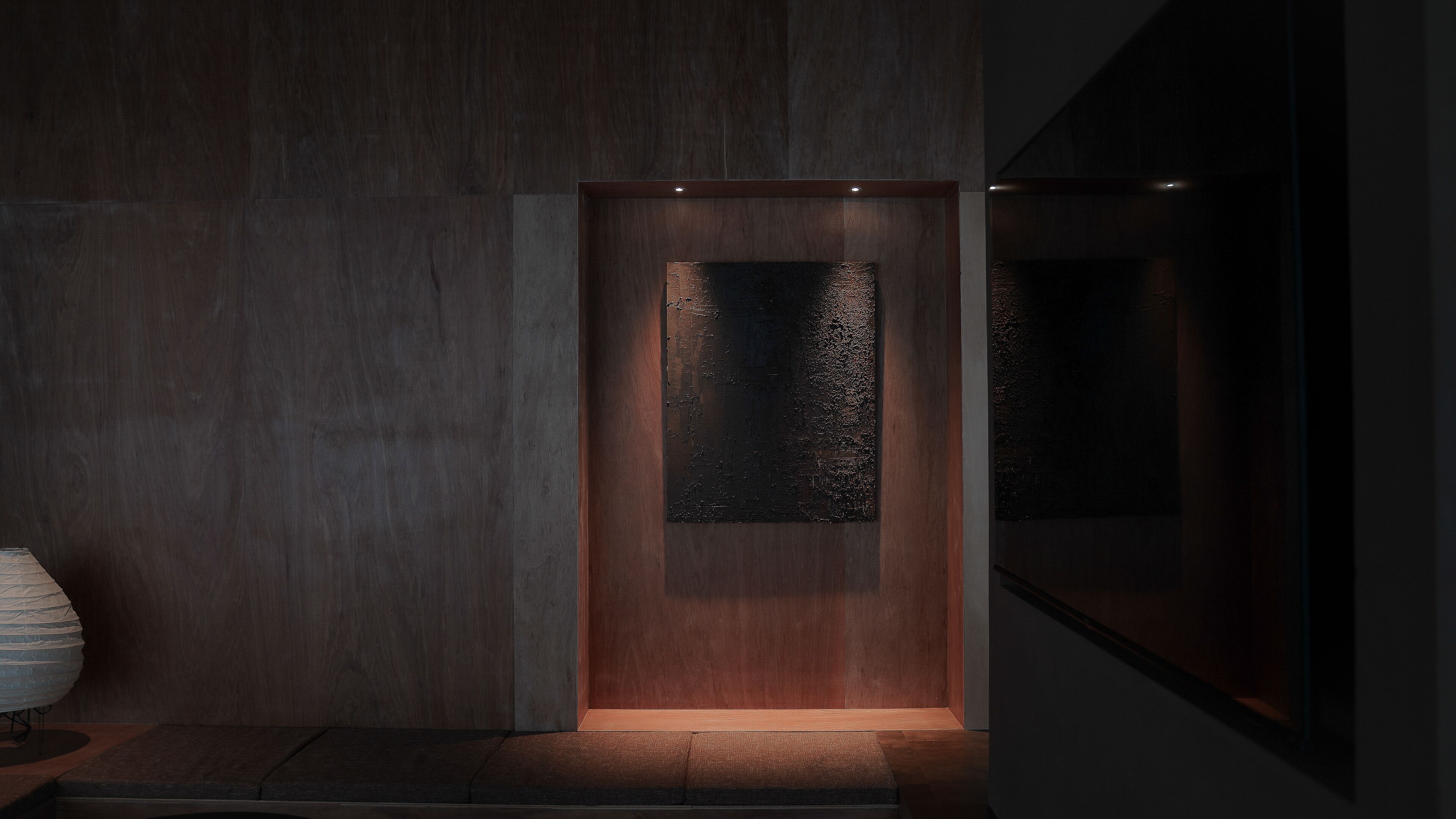A modern interior with a wooden panel wall, a recessed area with a textured surface, and a small table with a lamp.
