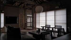 Un interior moderno con un sofá, una mesa de comedor con sillas, un ventanal con persianas verticales y un farolillo de papel colgante.