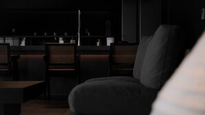 Un interior oscuro con una zona de bar, dos sillas de mimbre y un sofá.