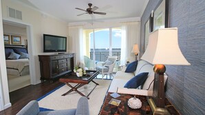A living room with a television, a ceiling fan, a sofa, a coffee table, and a view of the outdoors. - The Palm Tree Penthouse (Stuart)