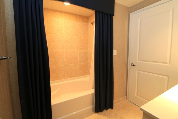 A bathroom with a bathtub, a door, and a curtain. - The Palm Tree Penthouse (Stuart)