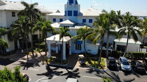 A hotel with a central tower, multiple palm trees, and a parking area with several cars. - The Palm Tree Penthouse (Stuart)