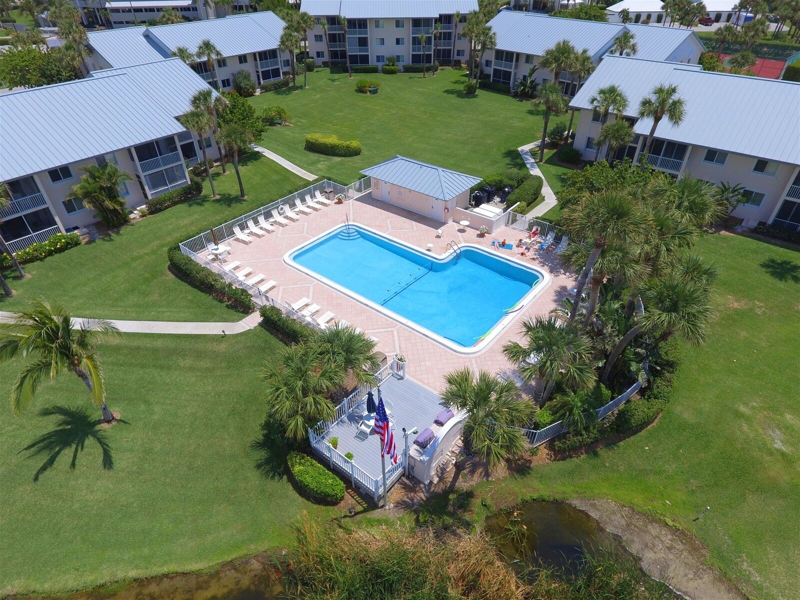 A pool surrounded by a deck with lounge chairs, a flag, and a small bridge.