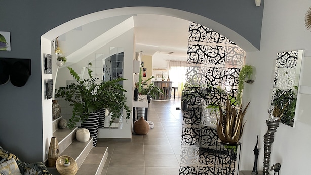 Een modern interieur met een gebogen witte boog die leidt naar een zithoek met een bank, potplanten en decoratieve vazen.